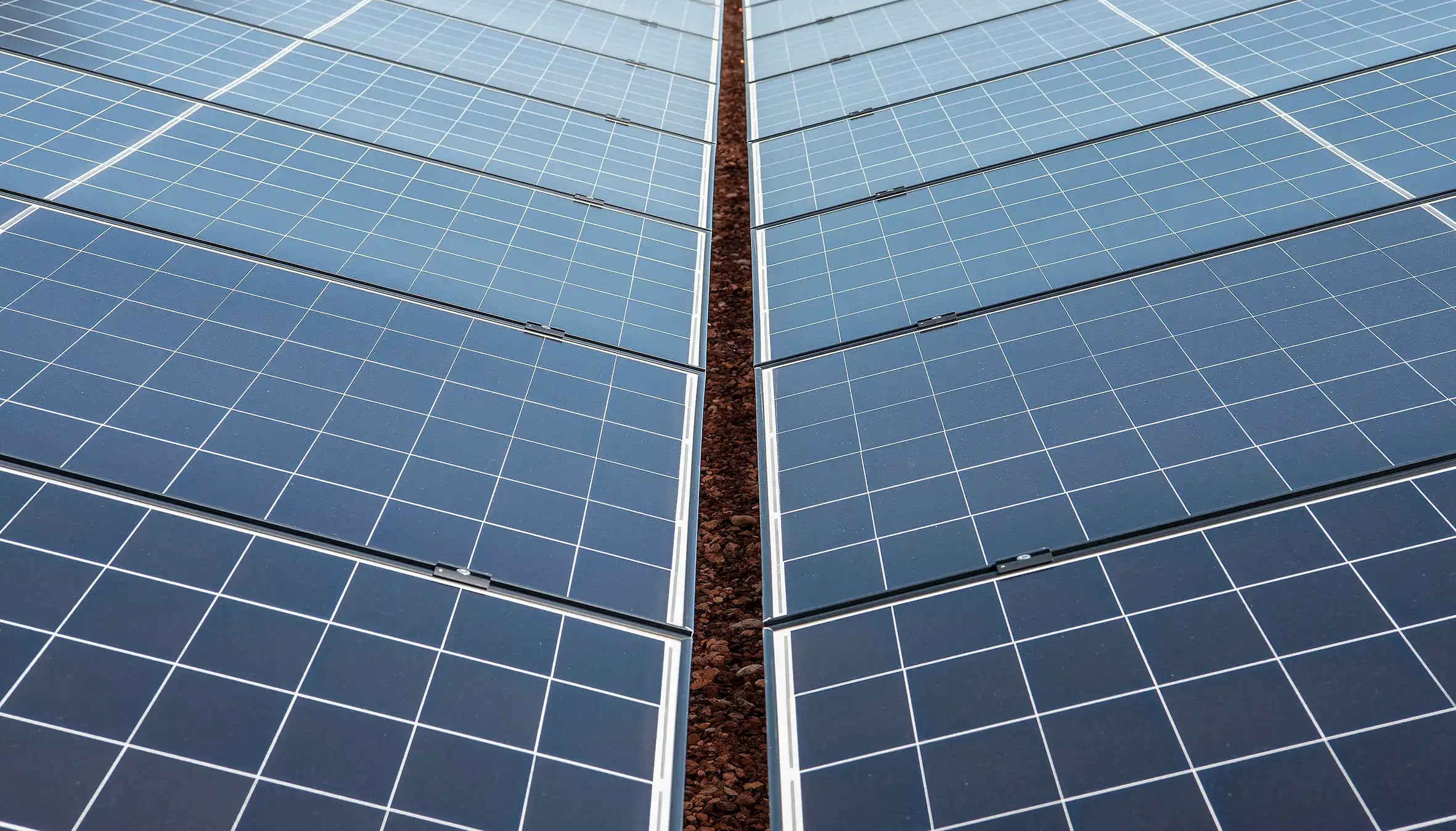 Rows of blue solar panels with a narrow, rocky gap between panels, converging toward the center.