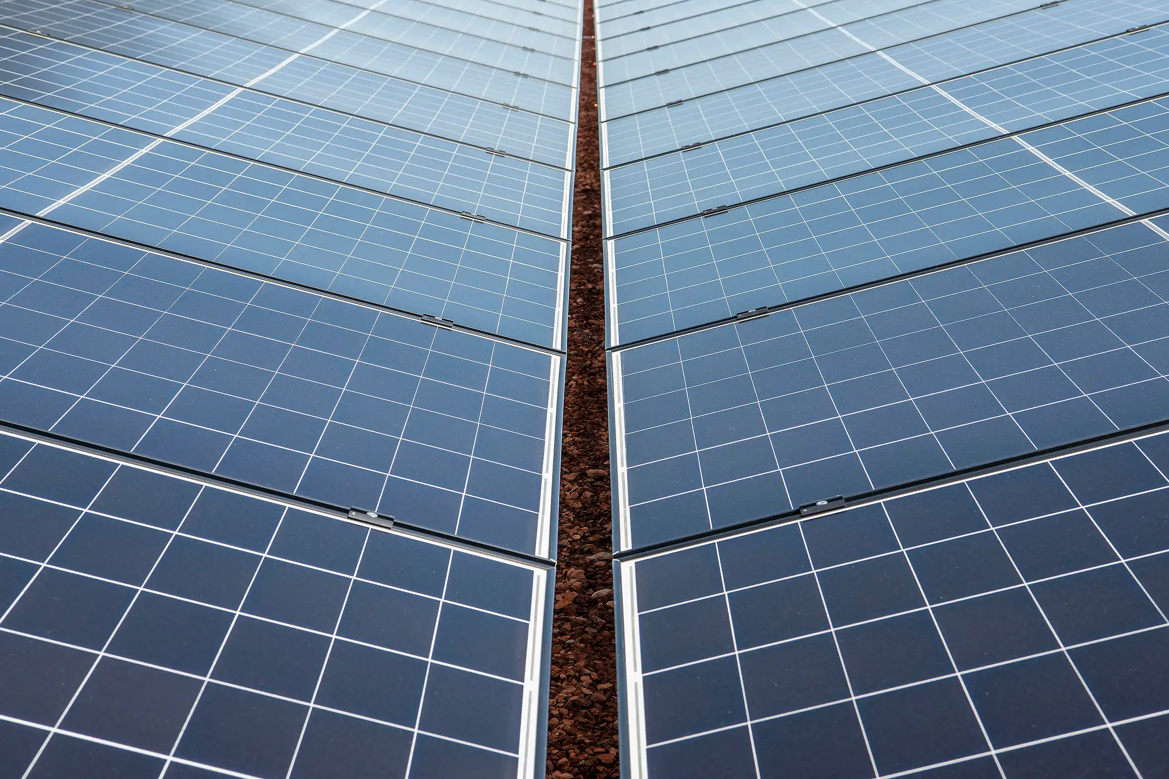 Rows of blue solar panels with a narrow, rocky gap between panels, converging toward the center.