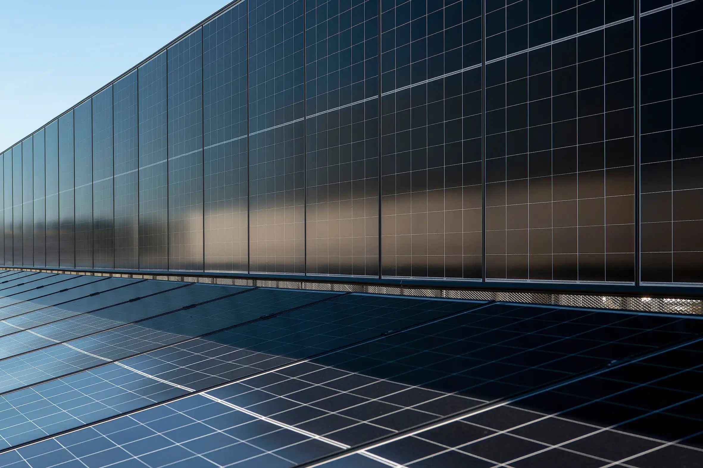 Facade covered with dark solar panels arranged in a grid under a clear blue sky.