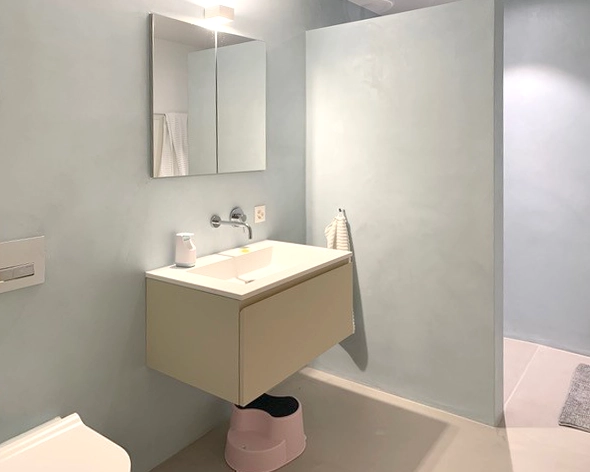 Floating beige vanity with white sink and wall-mounted faucet against pale blue walls, with a mirror and light above the sink.