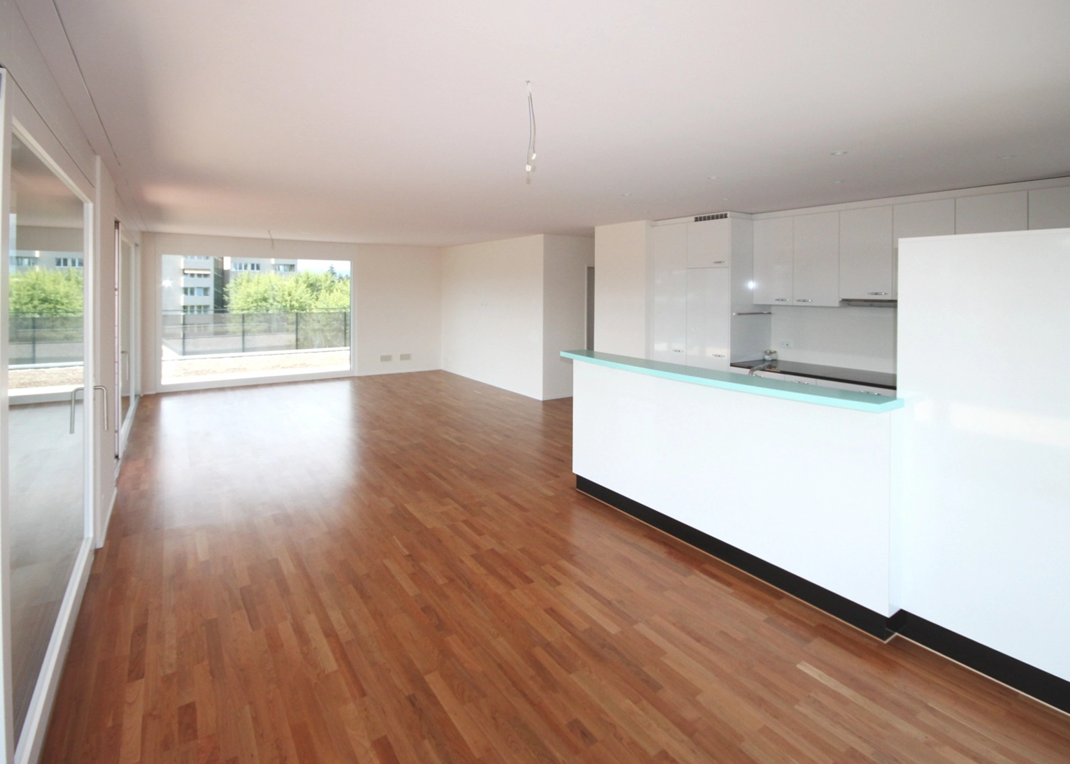 Spacious open-plan living area with wood flooring and a white curved kitchen island, large glass doors to a balcony.