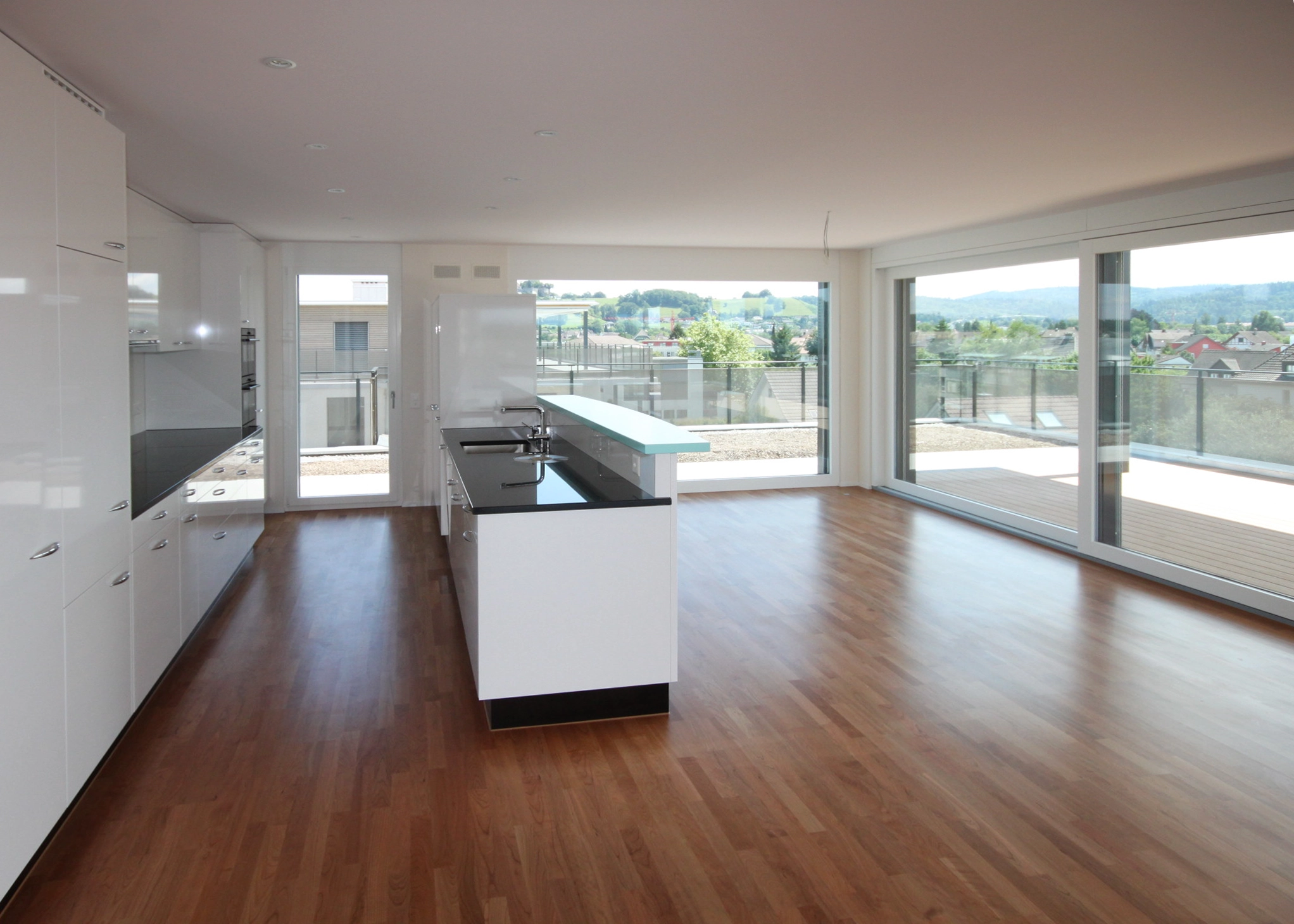 Bright modern kitchen with white cabinets, an island, and large glass doors opening to a hillside view.