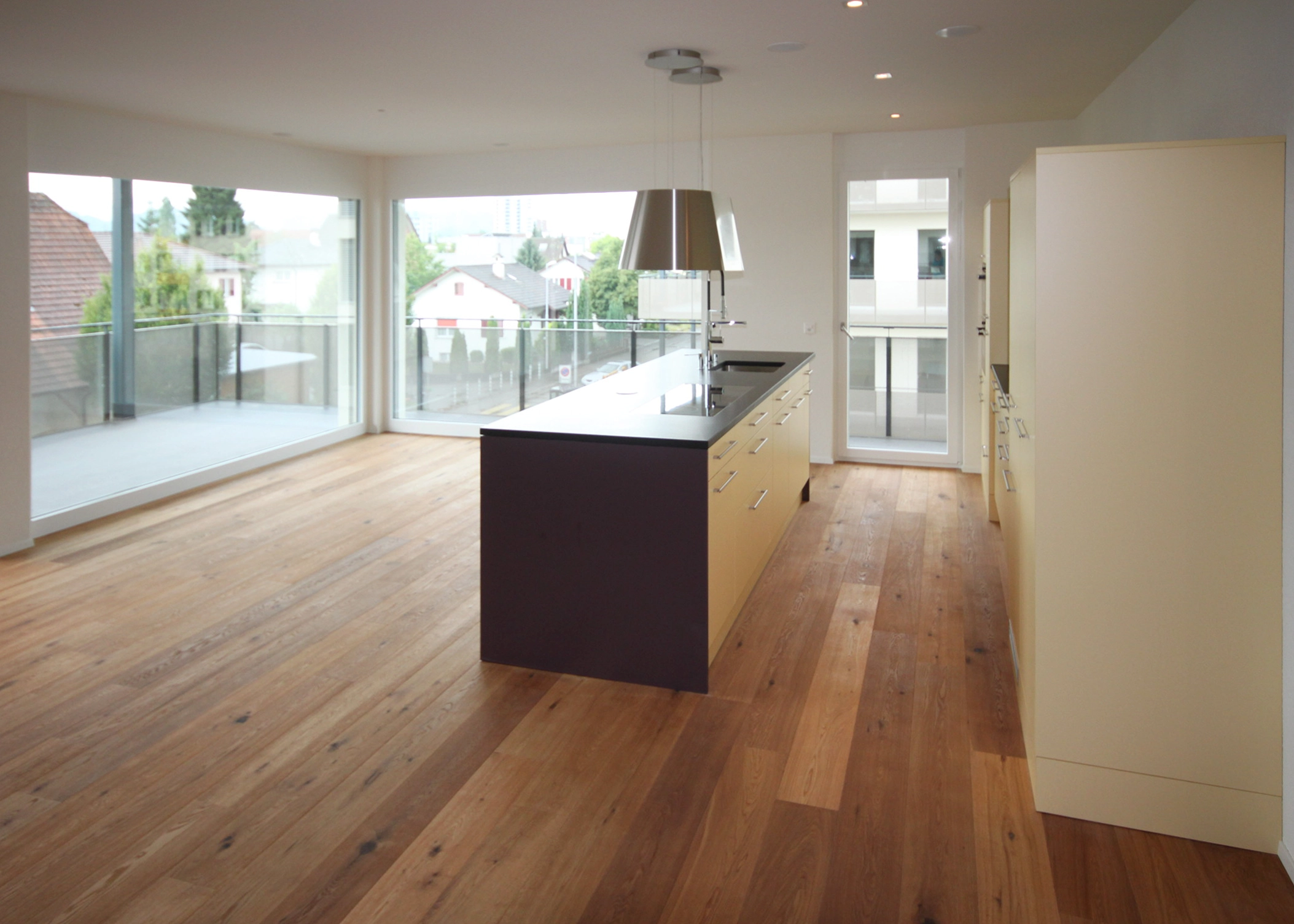 Bright modern kitchen with a central island, stainless steel fixtures, and expansive glass walls offering an urban view behind a balcony railings.
