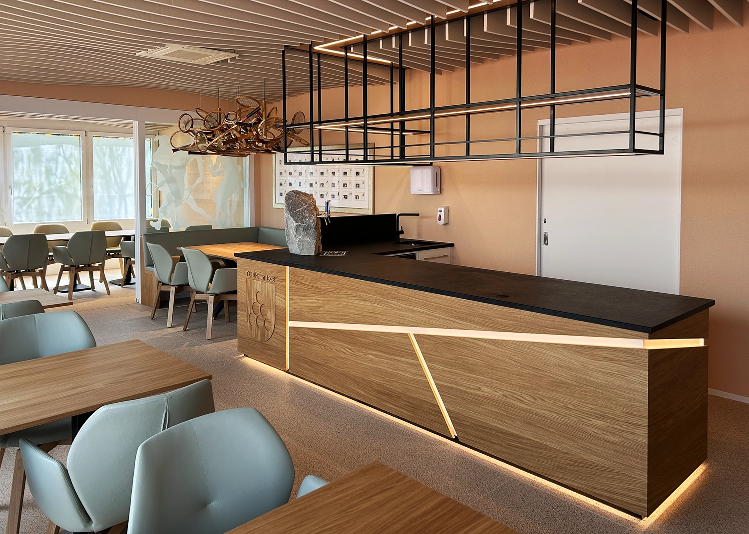 Modern café reception area with a long wooden counter, black metal ceiling frame, and a stone centerpiece on the counter.