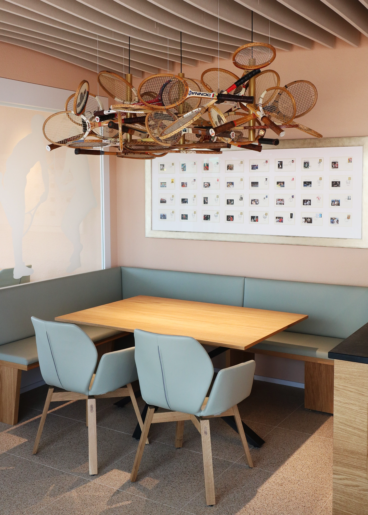 Chandelier made from piled vintage tennis rackets hangs from the ceiling over a wooden dining table with light blue chairs in a pastel-toned room