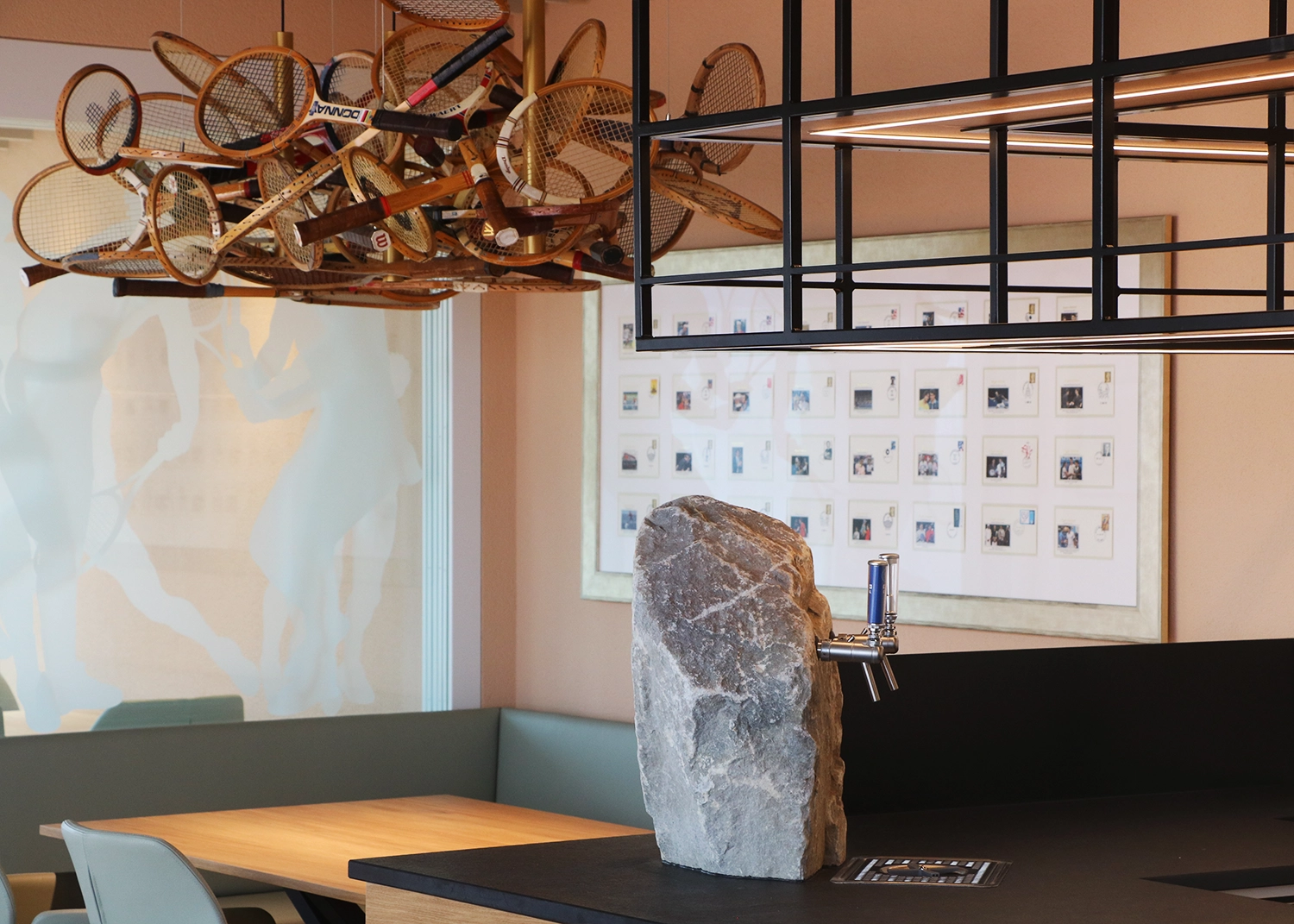 Decorative installation of old tennis rackets hanging from the ceiling above a seating area in a cafe.