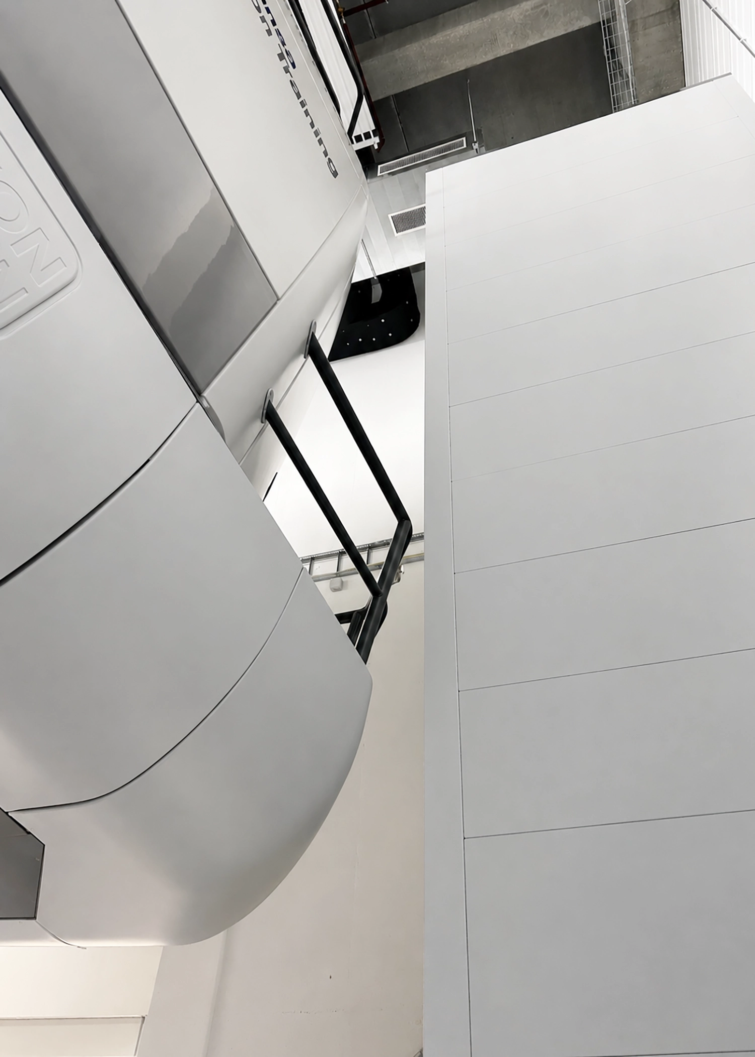 Interior of a modern building showing a large curved white wall with a black handrail and gray paneling, ceiling details visible.