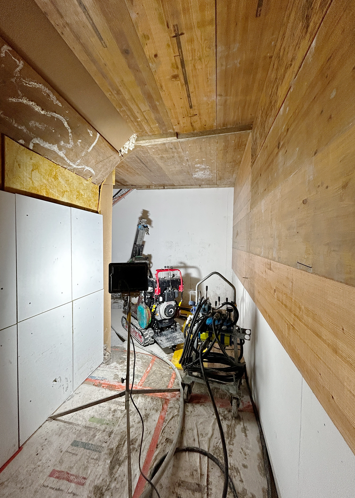Narrow unfinished utility room with wooden walls and ceiling, filled with tools, hoses and a small portable generator.