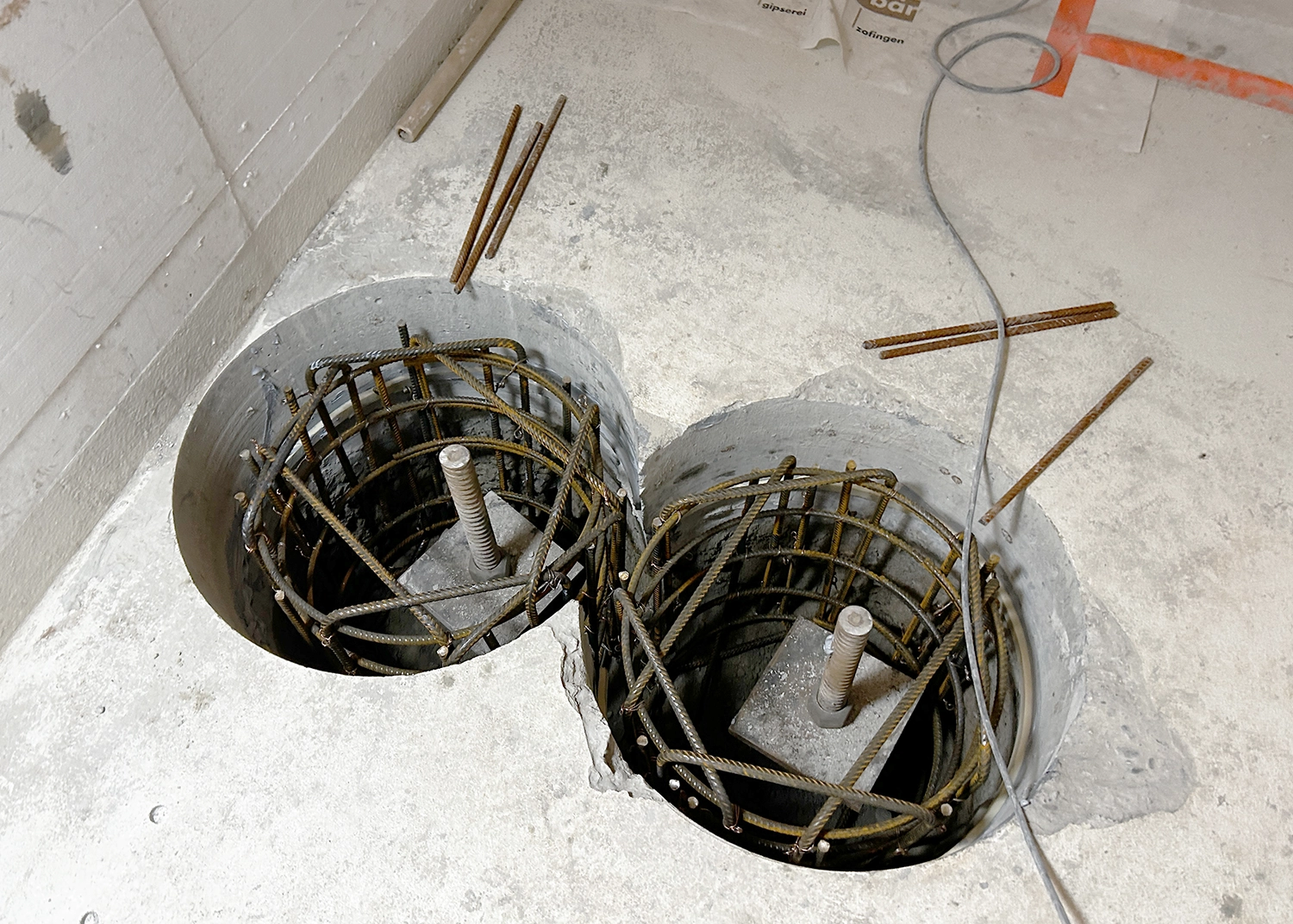 Concrete floor with two circular cores showing exposed steel rebar cages and formwork, wired for construction